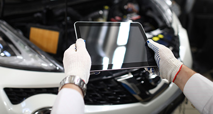 a person holding a tablet in front of the engine of a car