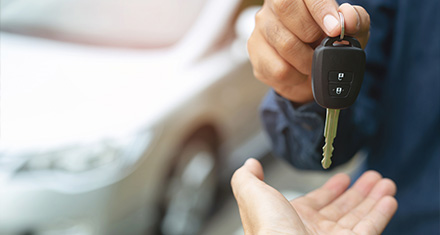 a person handing over car keys to a customer with a silver car in the background