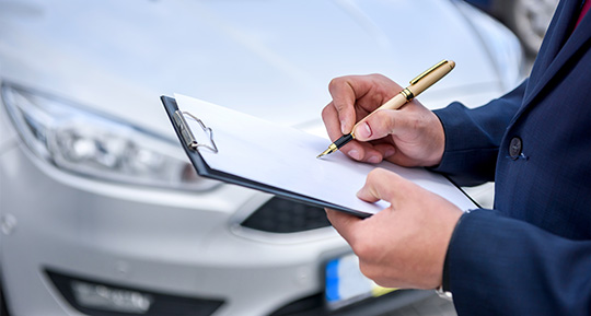 a person writing on a clipboard in front of a silver car