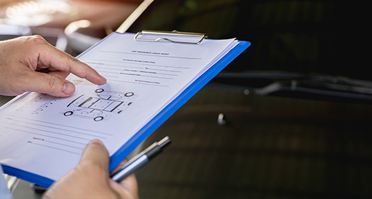 a person holding a clipboard and pointing at a section in front of a black car