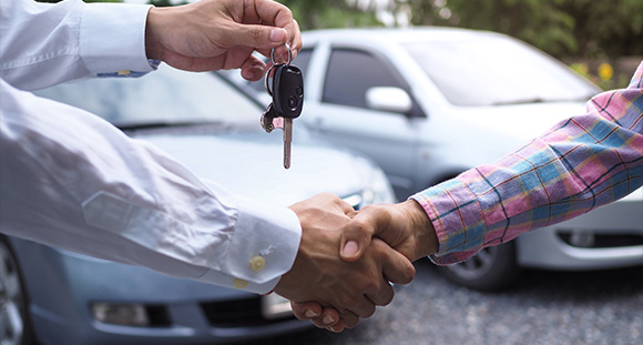 a car salesman shaking hands with a customer and handing over the keys for a new car