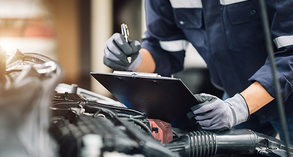 a person with a clipboard performing an integrity check on the engine of a car